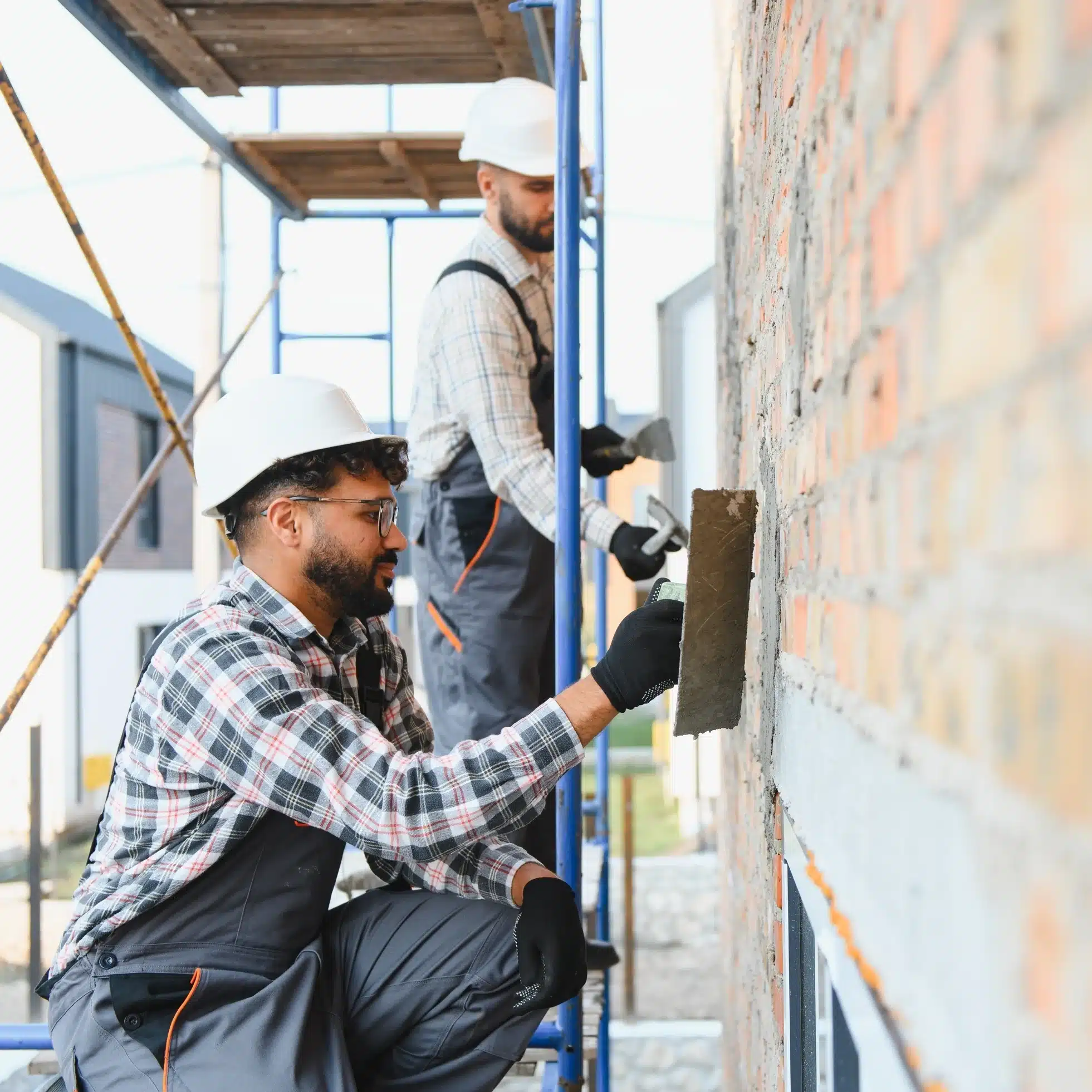 Rénovation façade maison : échafaudage et chantier Chantier de rénovation extérieure d'une maison moderne, échafaudages métalliques devant les façades couleur crème sous un ciel bleu avec nuages.