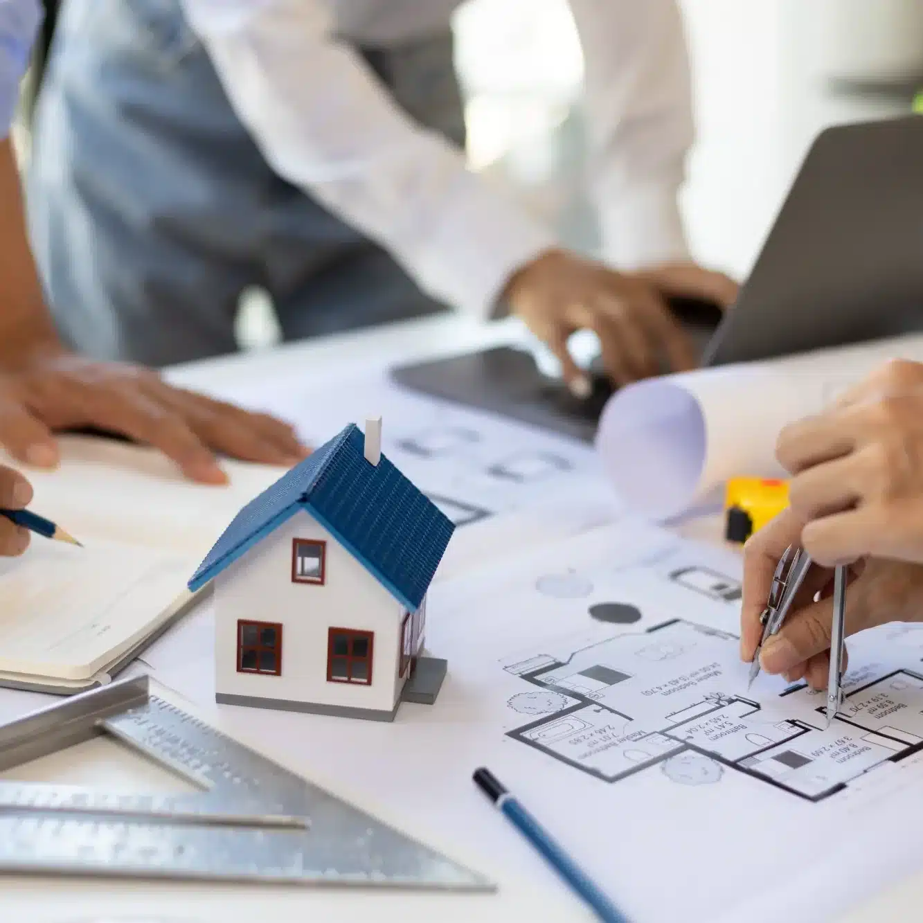 Architectes planifiant un projet de maison. Maquette, plans d'étage détaillés et outils de conception (compas, ordinateur) sur la table de travail.