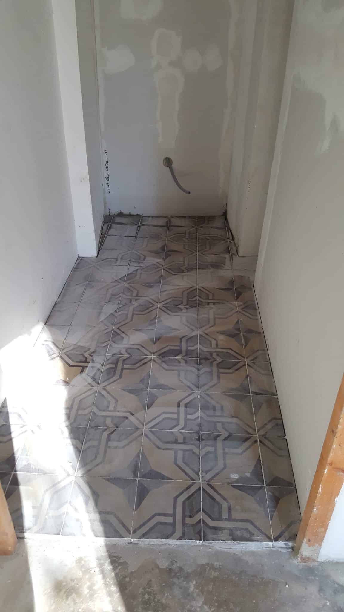 Pose de carrelage géométrique dans un couloir étroit en travaux avec murs en placoplatre.