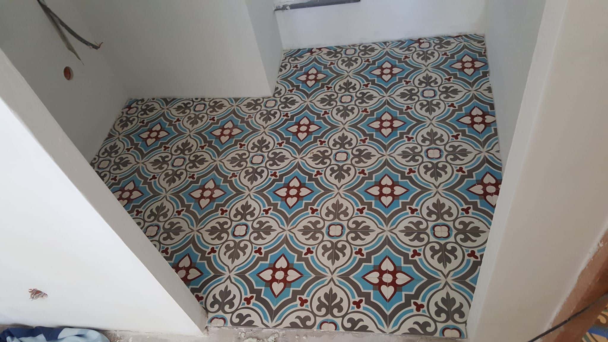 Carrelage aux motifs géométriques bleus et bordeaux sur le sol d'une pièce blanche en cours de rénovation.