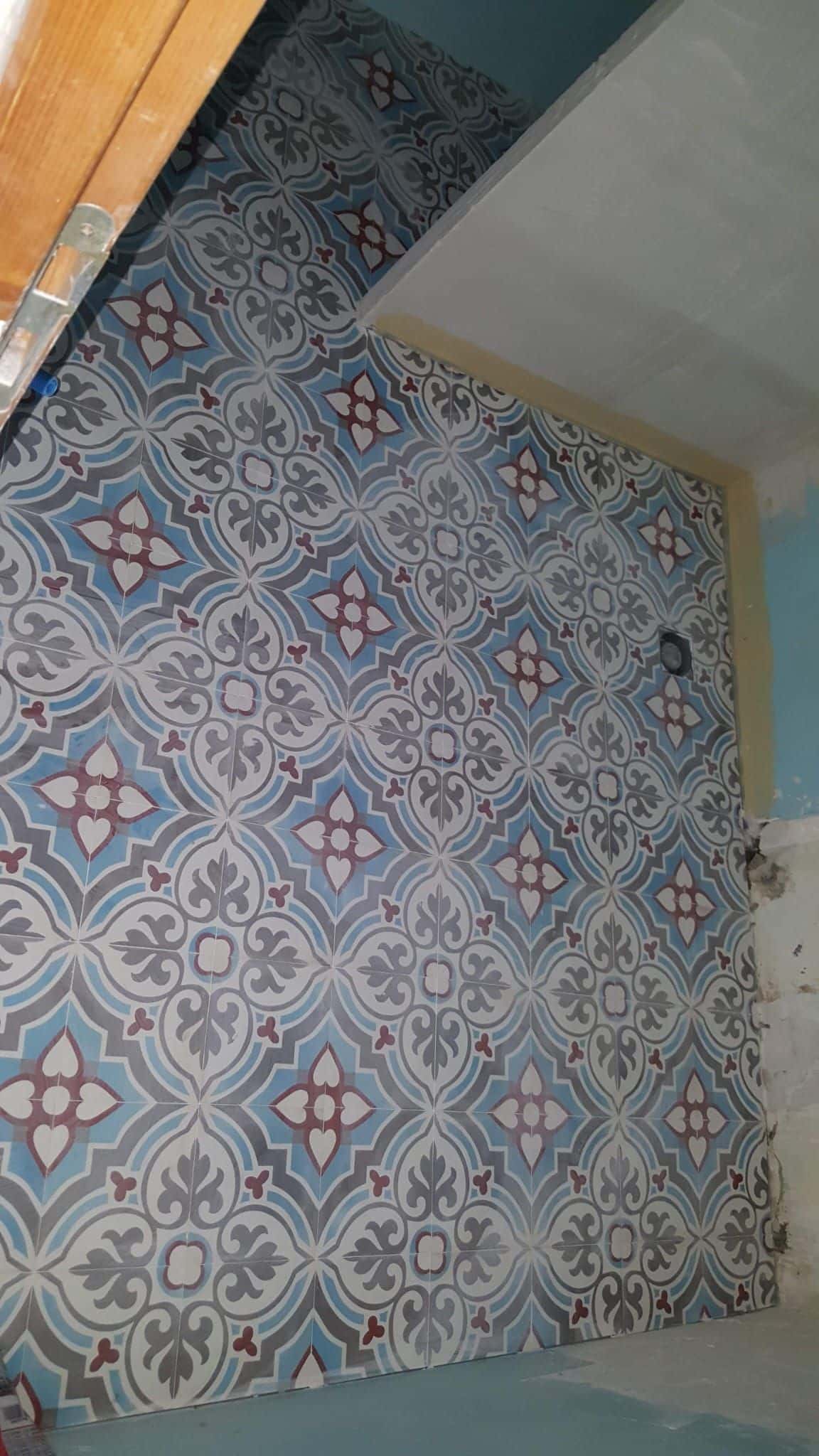 Carrelage mural aux motifs bleus, gris et rouges dans une pièce en cours de rénovation avec cloison sèche.