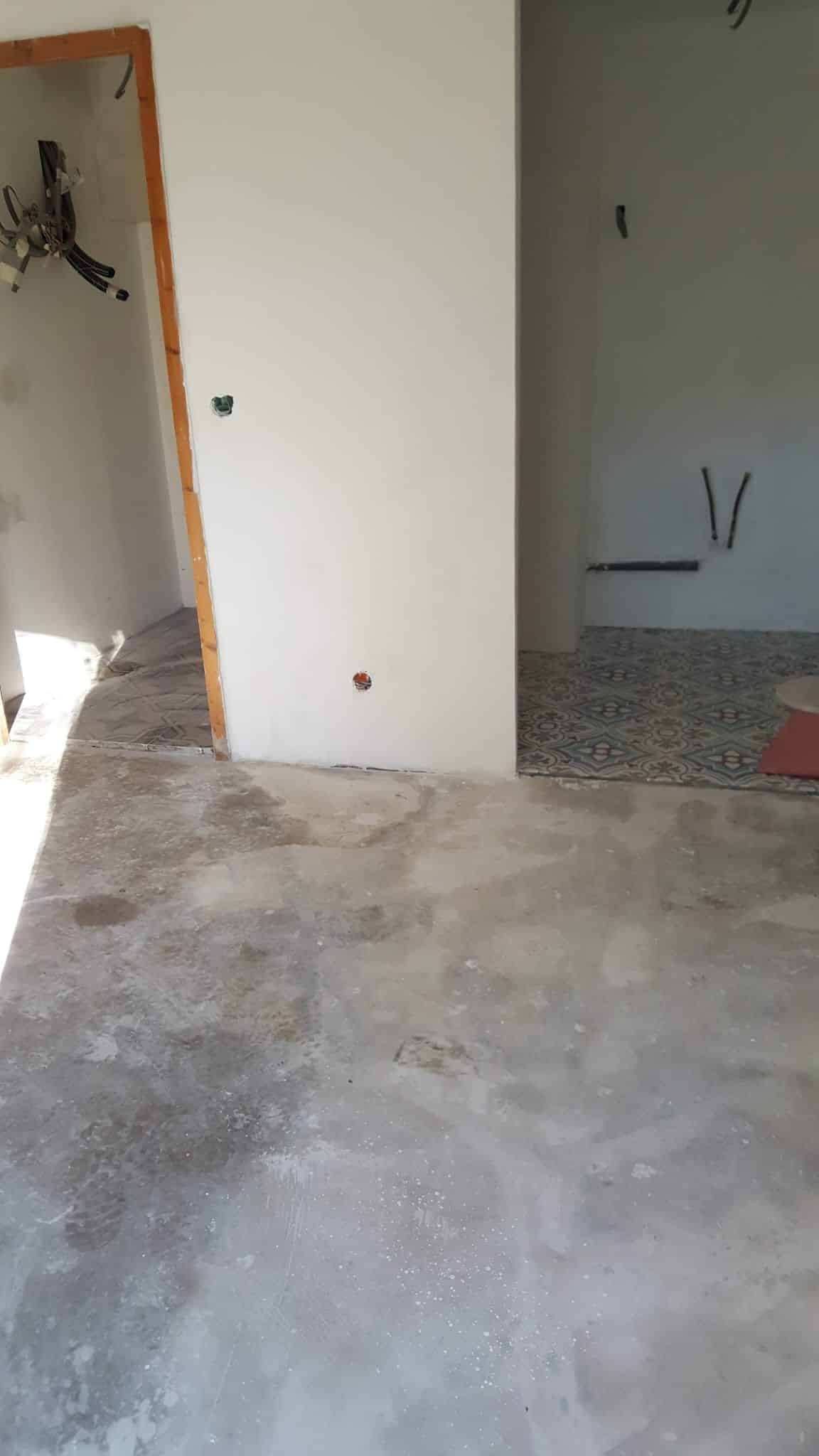 Intérieur en rénovation avec sol en béton, murs blancs, câblage électrique et carrelage décoratif au fond.
