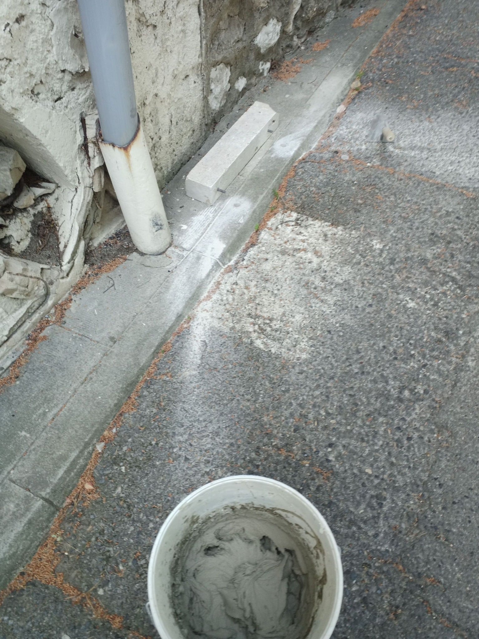 Seau de mortier frais prêt pour la réparation d'un mur extérieur en pierre avec bloc de béton.