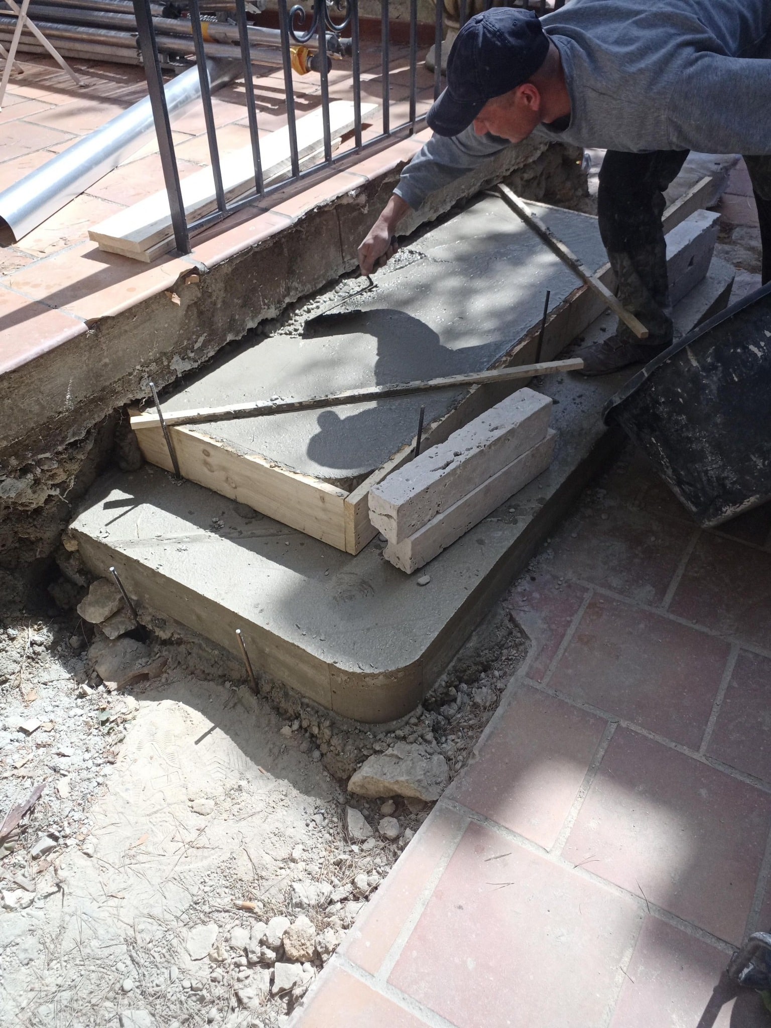 Maçon lissant du béton frais pour une marche d'escalier extérieure avec un coffrage en bois et une truelle.